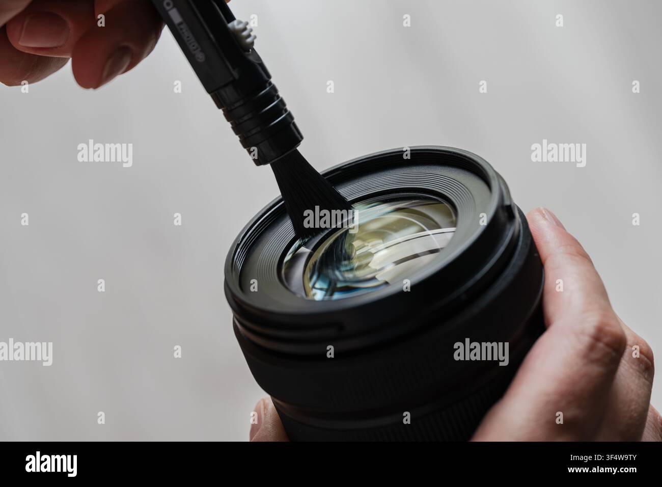 Mano che utilizza una spazzola specializzata per pulire l'elemento anteriore di una lente della fotocamera Foto Stock