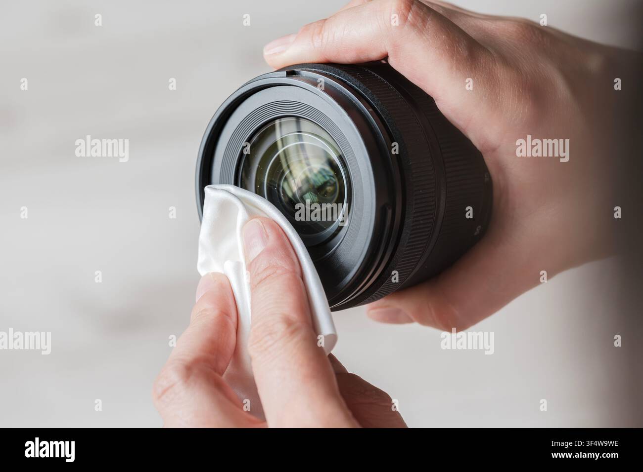 Le mani di una persona puliscono con cura una lente della fotocamera con un panno in microfibra bianco Foto Stock