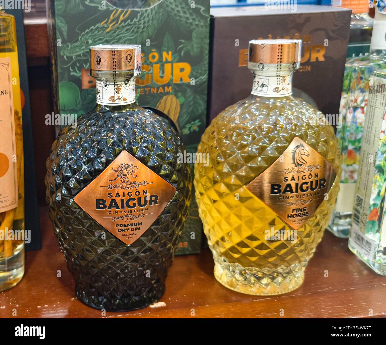 Bottiglie di gin artigianale vietnamita premium Saigon Baigur con vetro a motivo a diamanti distinto ed etichette a forma di scudo su una mensola di legno Foto Stock