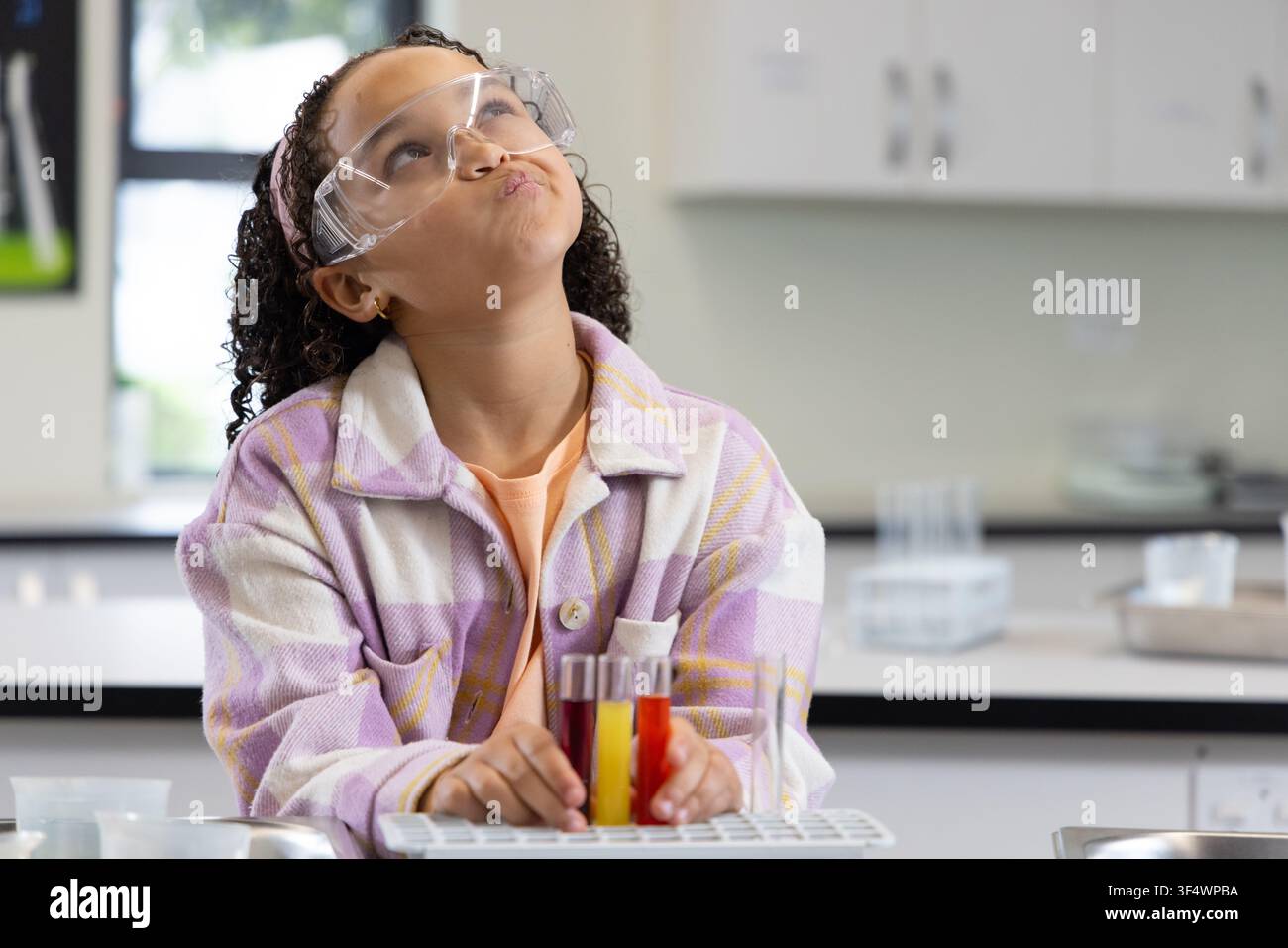 Studente afroamericano giovane seduto in un laboratorio con occhiali da laboratorio che tiene una rastrelliera con tre provette Foto Stock