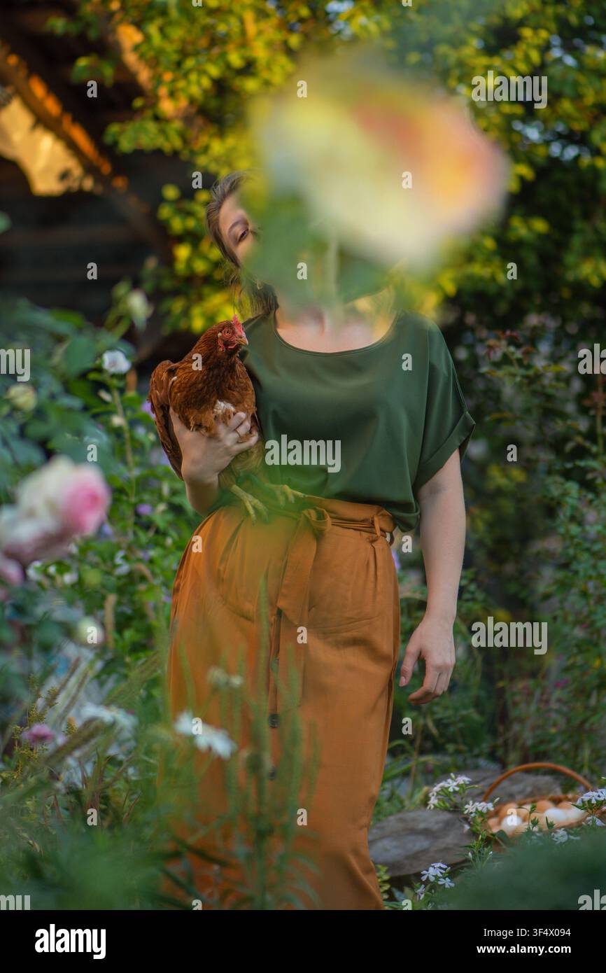 Coltura ragazza tiene una gallina marrone vicina nel giardino sul retro. Allegra agricoltrice che tiene la gallina tra le mani nella fattoria. Foto Stock