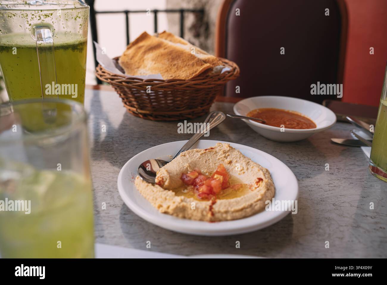 Hummus con olio d'oliva e pomodori a dadini, servito con pane pita e bevande fredde verdi Foto Stock