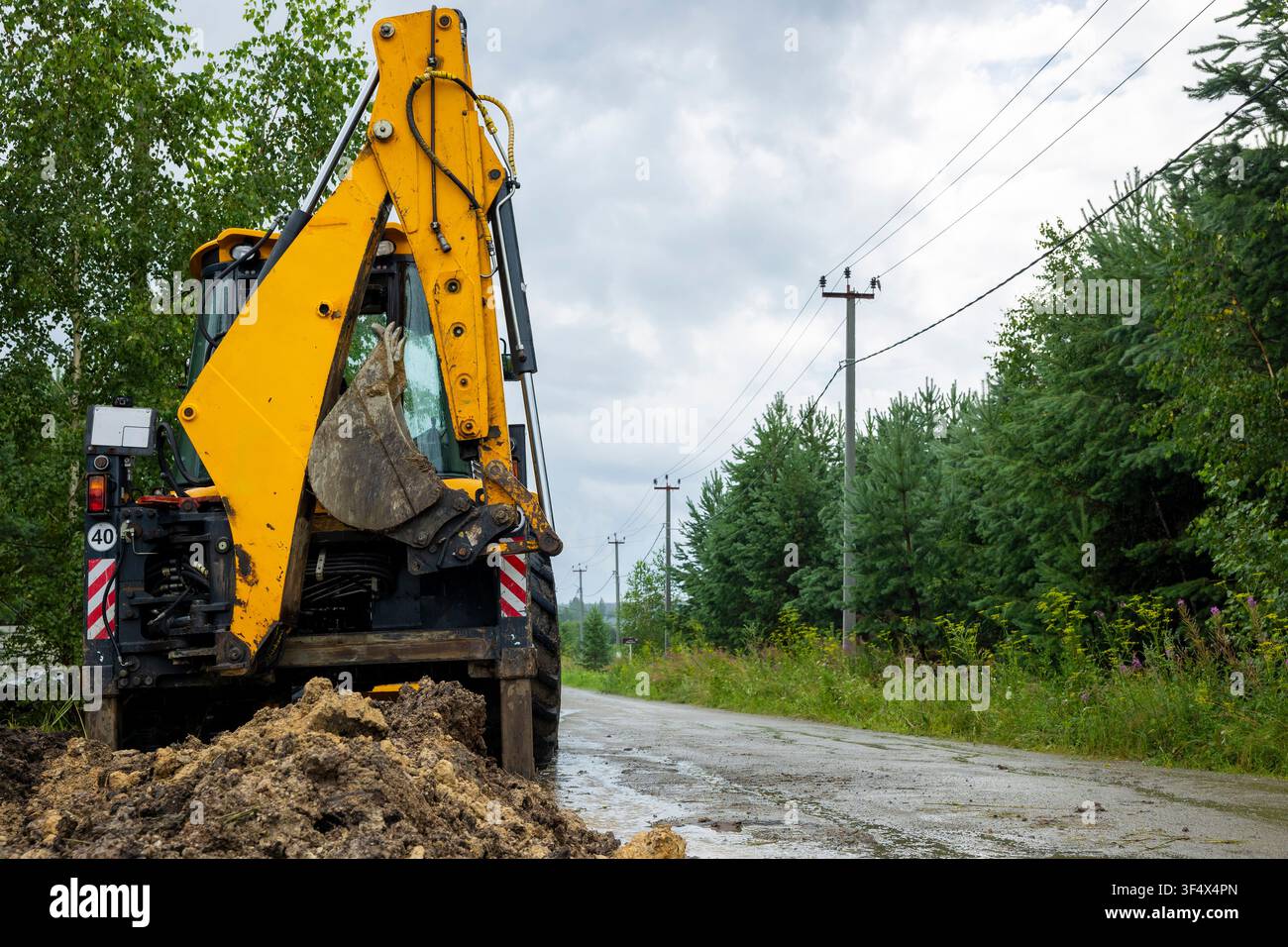 Caricatore con braccio idraulico parcheggiato accanto a una strada rurale dopo lavori di scavo. Concetto: costruzione utilitaria Foto Stock
