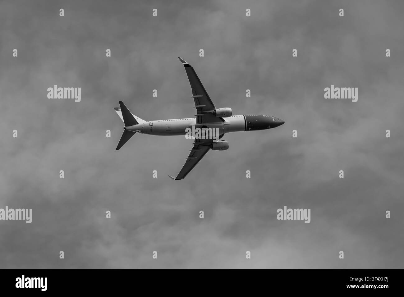 Aereo passeggeri commerciale che si muove sopra le nuvole del cielo in bianco e nero, simboleggiando il trasporto globale e l'aviazione civile Foto Stock