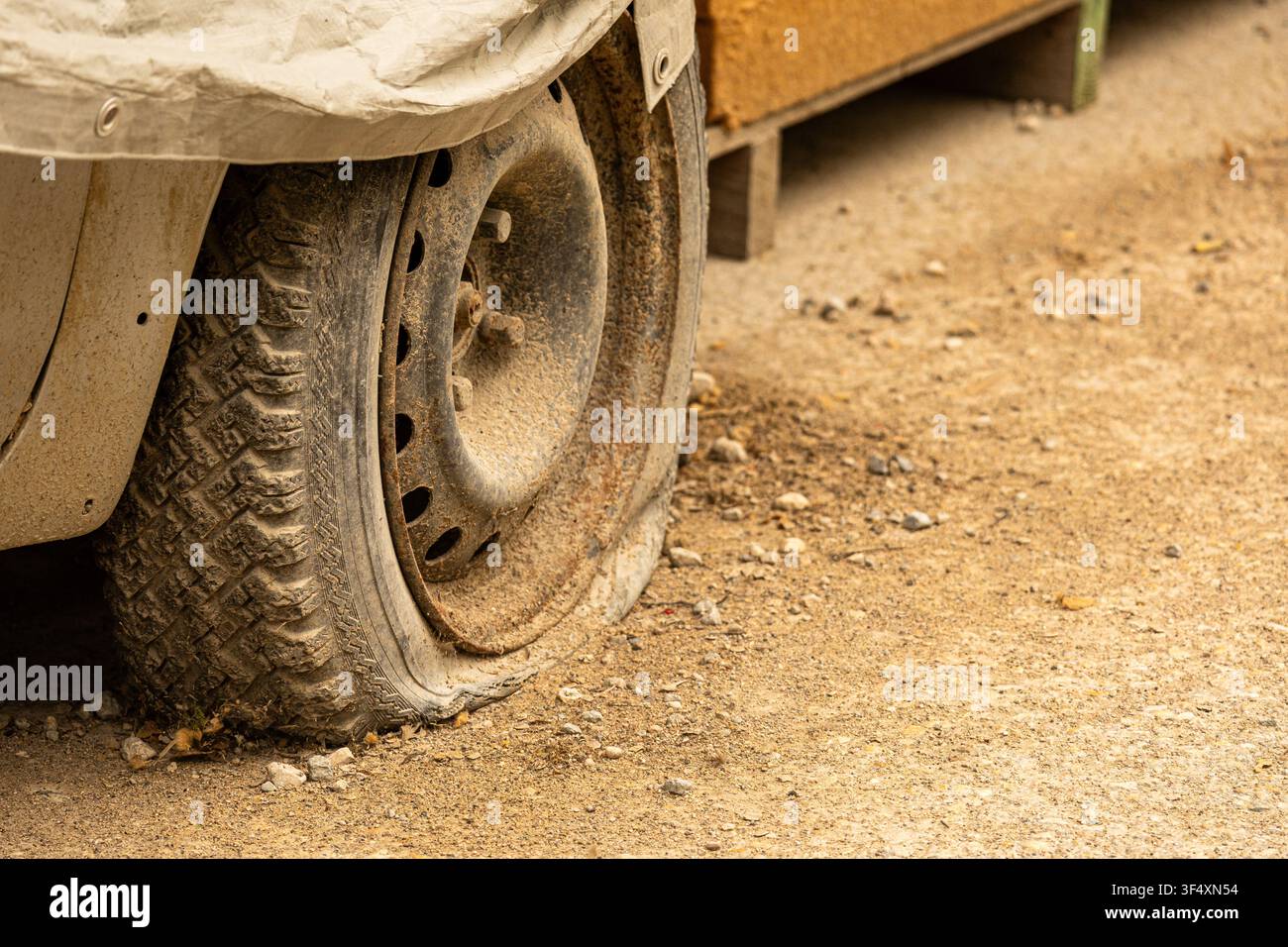 Primo piano di una gomma a terra su un veicolo parcheggiato con uno sfondo di strada polverosa. Adatto per concetti di trasporto, guasto e manutenzione. Foto Stock