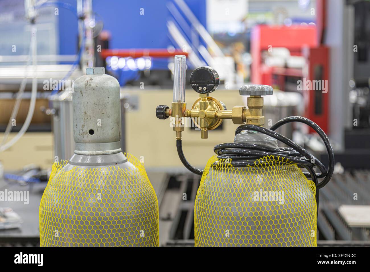 Bombole di gas industriali con rete protettiva gialla, valvole metalliche, regolatore in ottone, tubo nero, ambiente di officina ben illuminato, grigio metallico e y Foto Stock