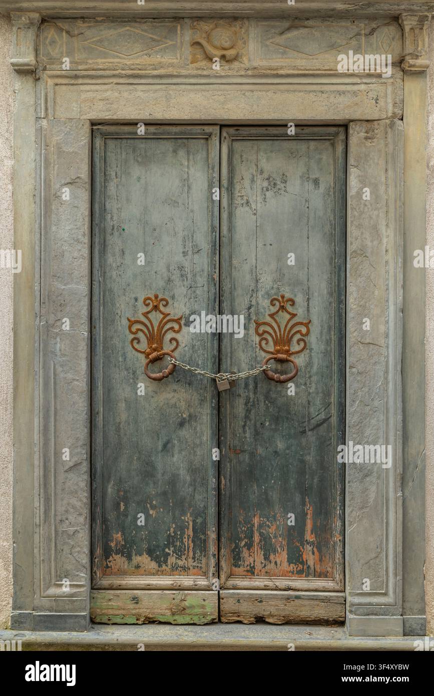 Porta di legno stagionata fissata da una catena e un lucchetto all'interno di una cornice in pietra Foto Stock