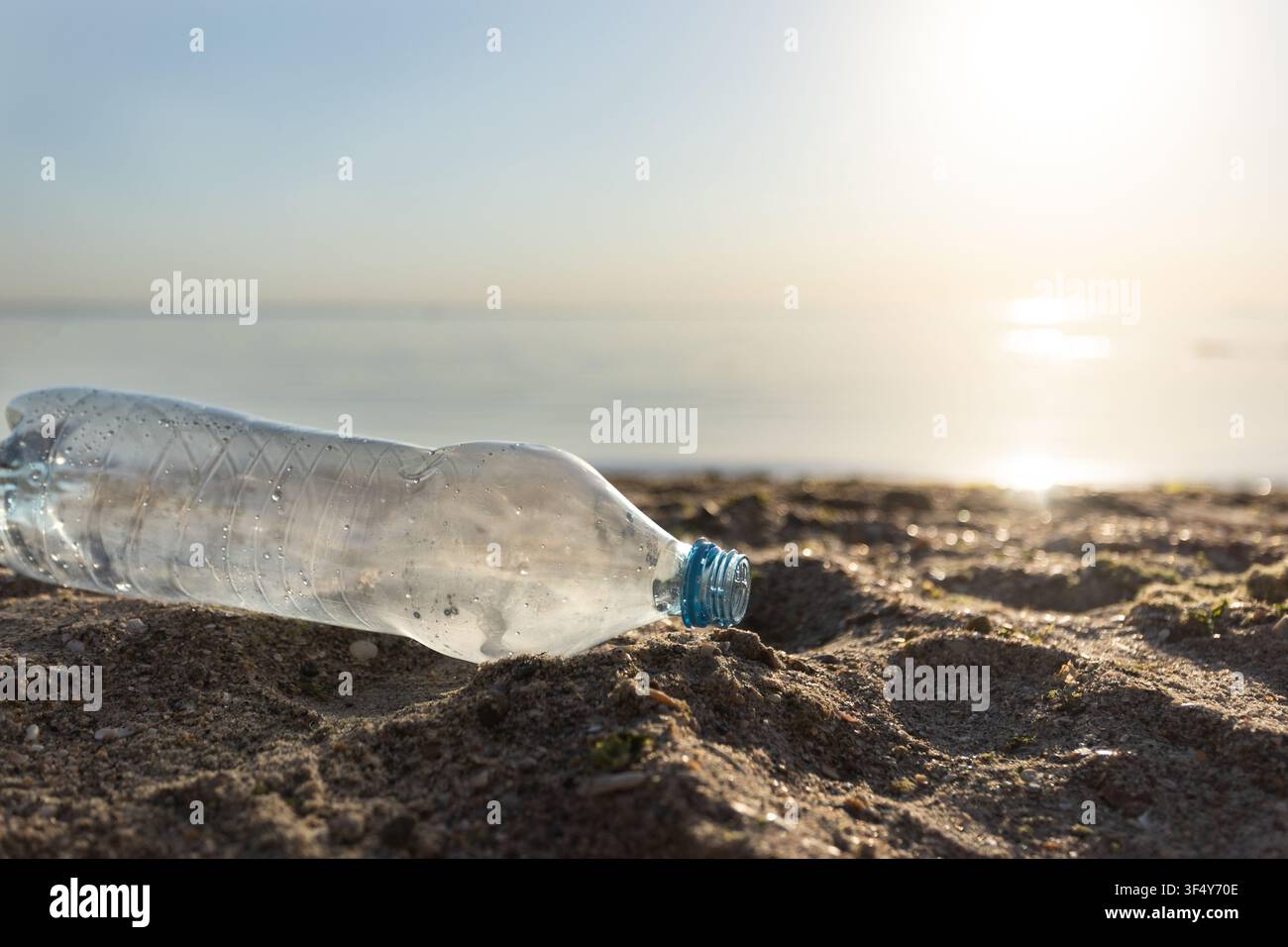Bottiglia di plastica sprecata che giace sulla spiaggia vicino all'acqua, sfondo ecologico Foto Stock