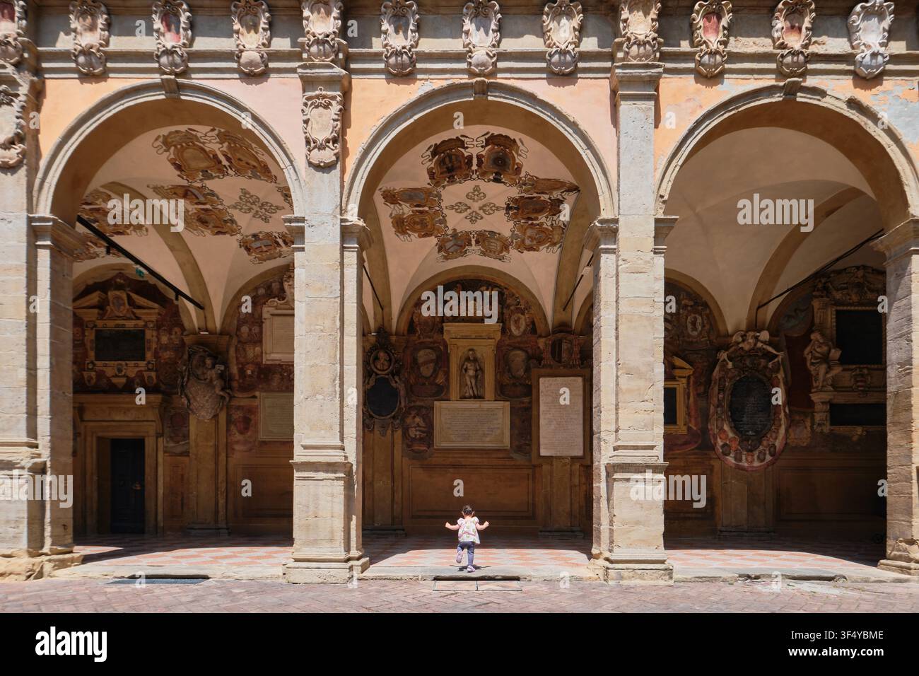 Bologna, Italia – Maggio 2026: Bambino che cammina attraverso il loggiato del cortile decorato con stemmi araldici nel Palazzo Archiginnasio Foto Stock
