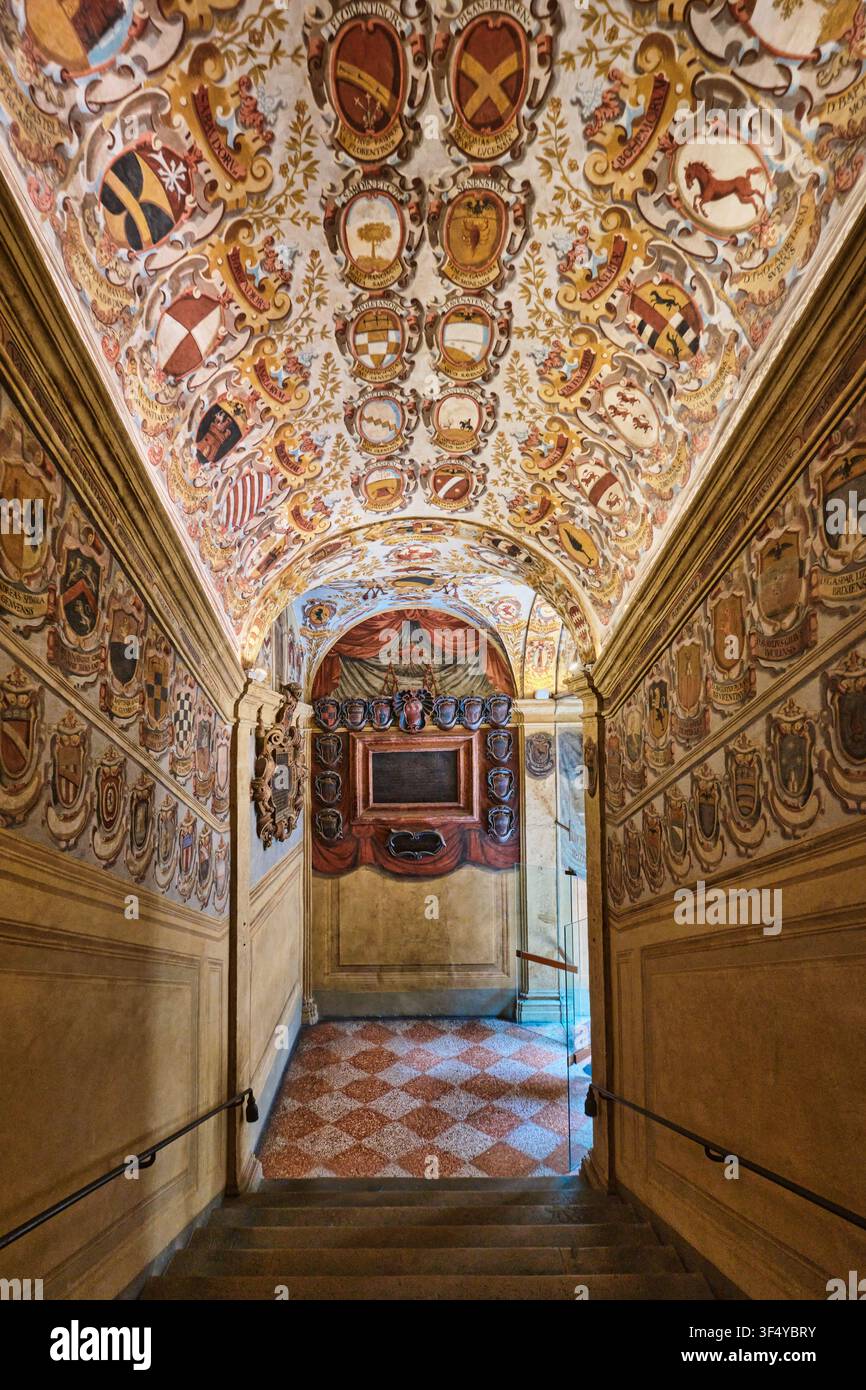 Bologna, Italia – Maggio 2026: Scala storica e soffitto a volta decorati con stemmi araldici nel Palazzo Archiginnasio Foto Stock