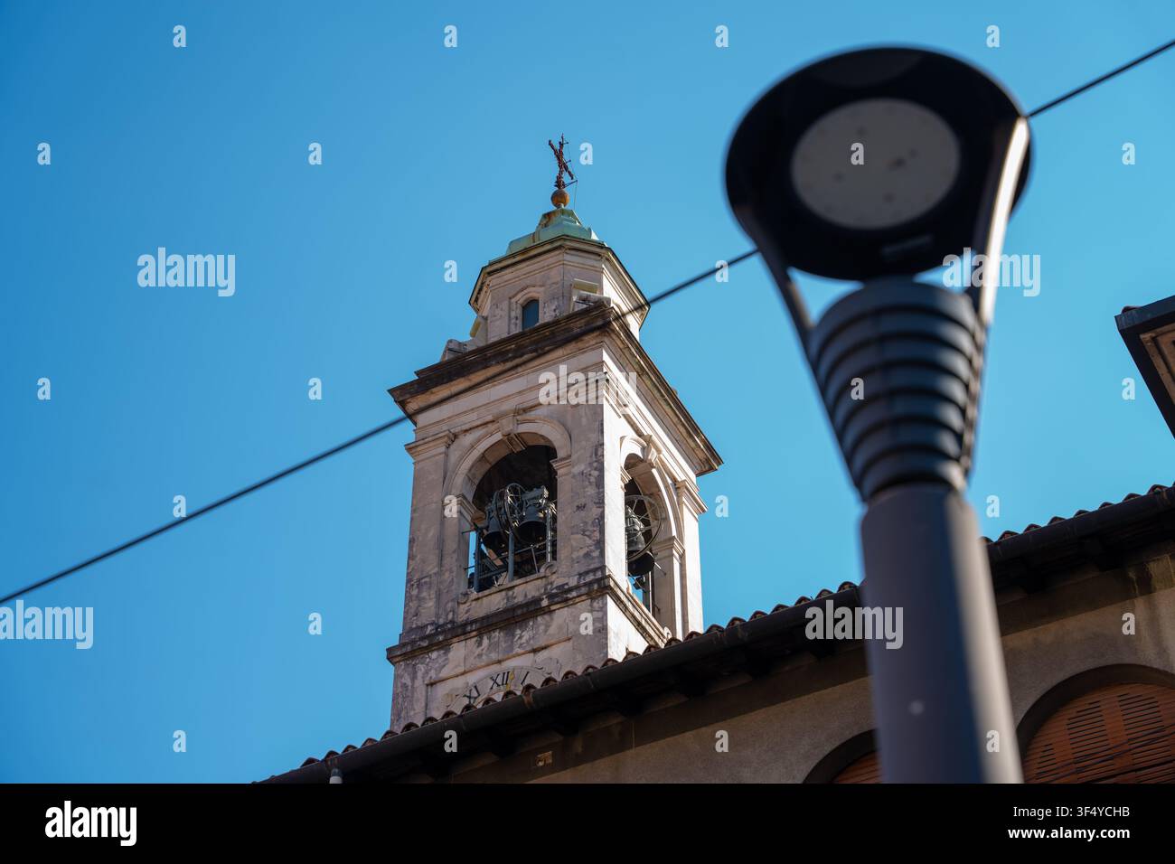 Bergamo, Italia - 16 giugno 2026: Scatto architettonico ad angolazione bassa di un antico campanile in pietra contro un cielo blu terso, incorniciato da un moderno sfocato Foto Stock