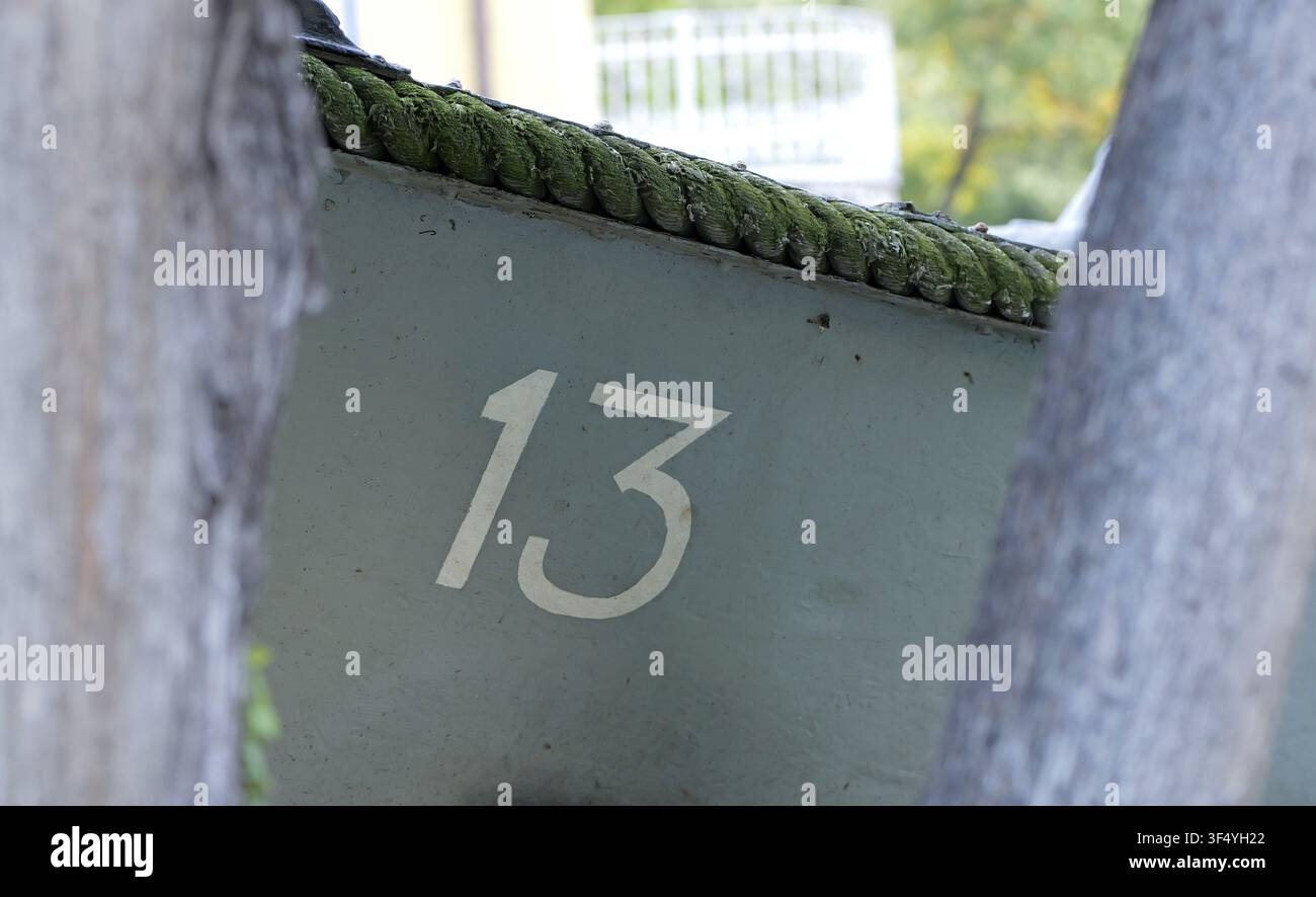 Il numero 13 dipinto in bianco sul fianco di uno scafo di barca consumato, con dettagli di una corda ricoperta di muschio verde lungo la murata, incorniciato da uno sfondo sfocato Foto Stock