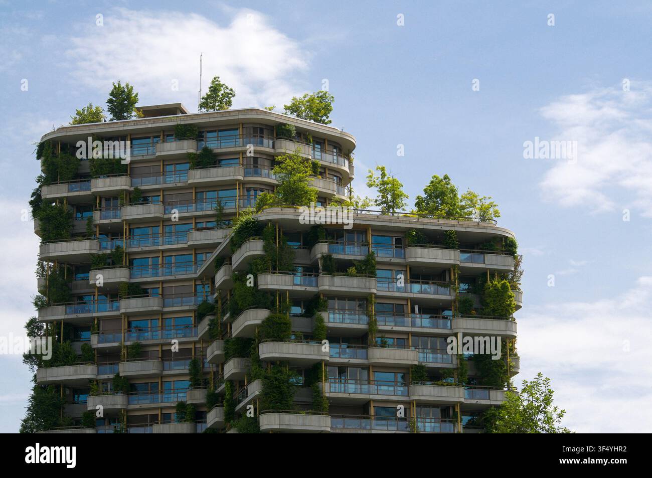 Vista ad angolo basso dei piani superiori di un grattacielo sostenibile moderno con giardini verticali rigogliosi, alberi, integrati nell'architettura Foto Stock