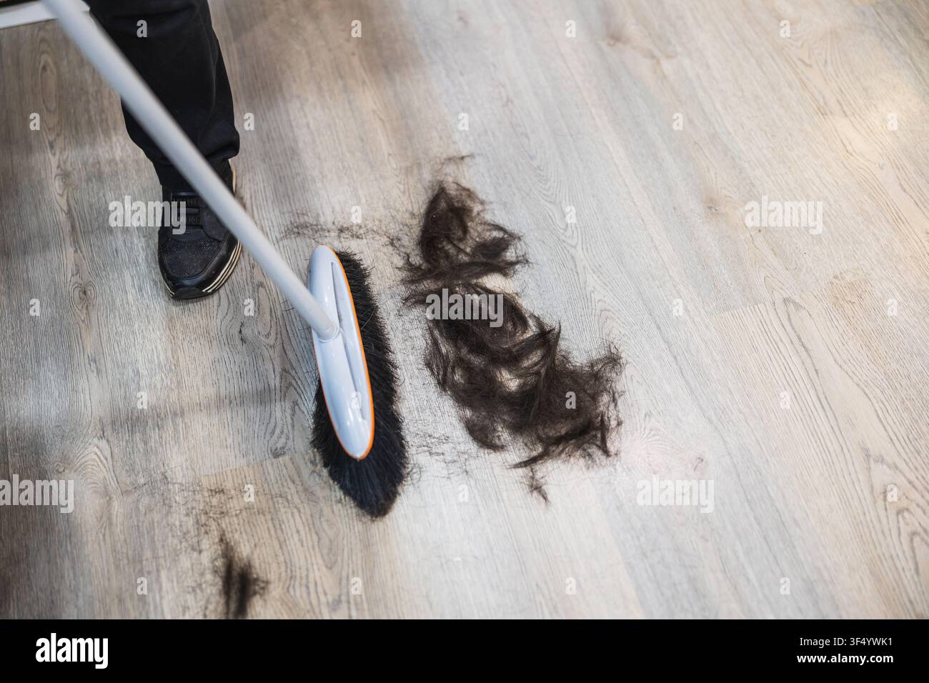 Parrucchiere che spazza i capelli tagliati dal pavimento del salone Foto Stock