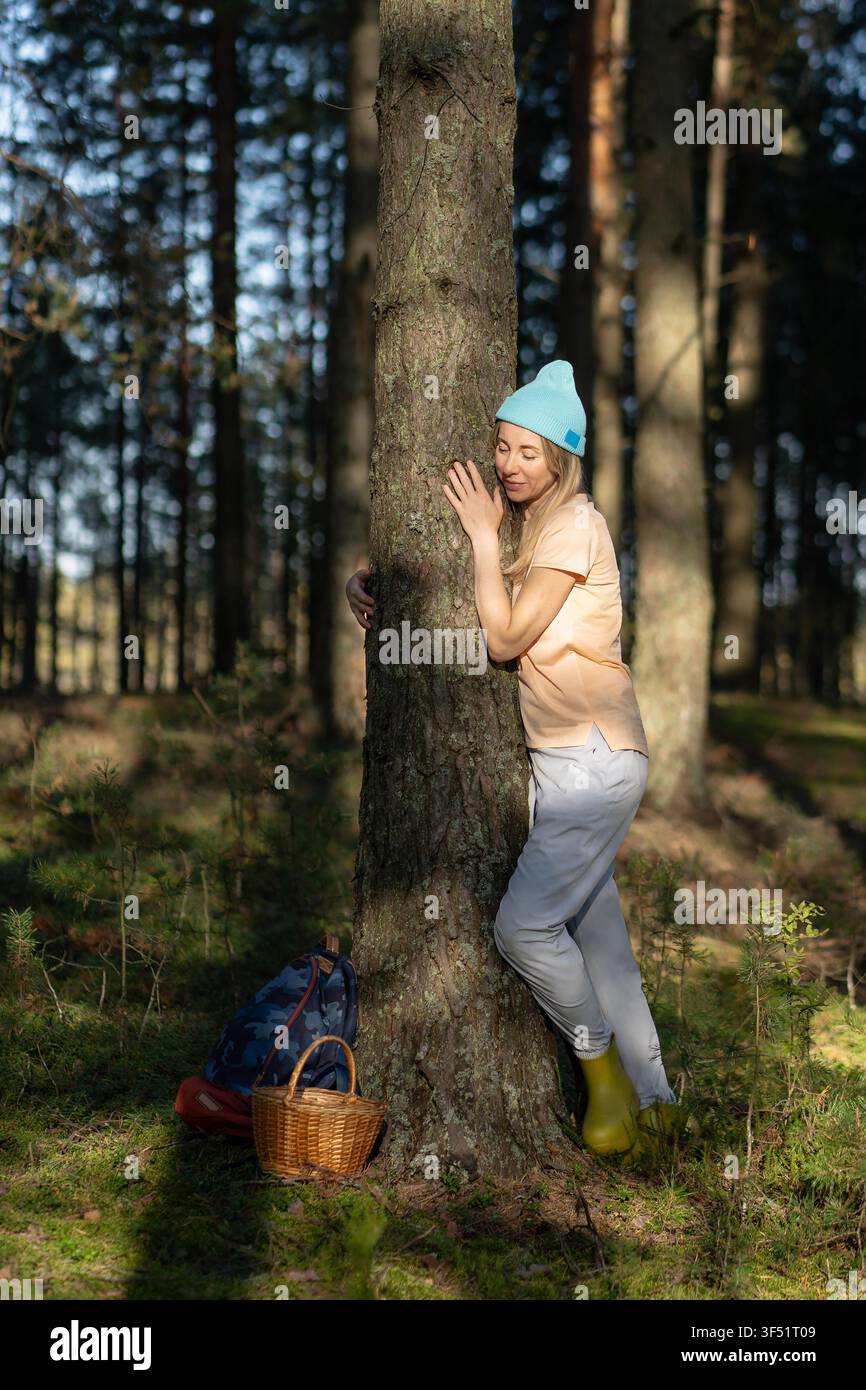 Donna che abbraccia l'albero durante la raccolta nei boschi. Pacifica connessione terrestre femminile, amante verde Foto Stock