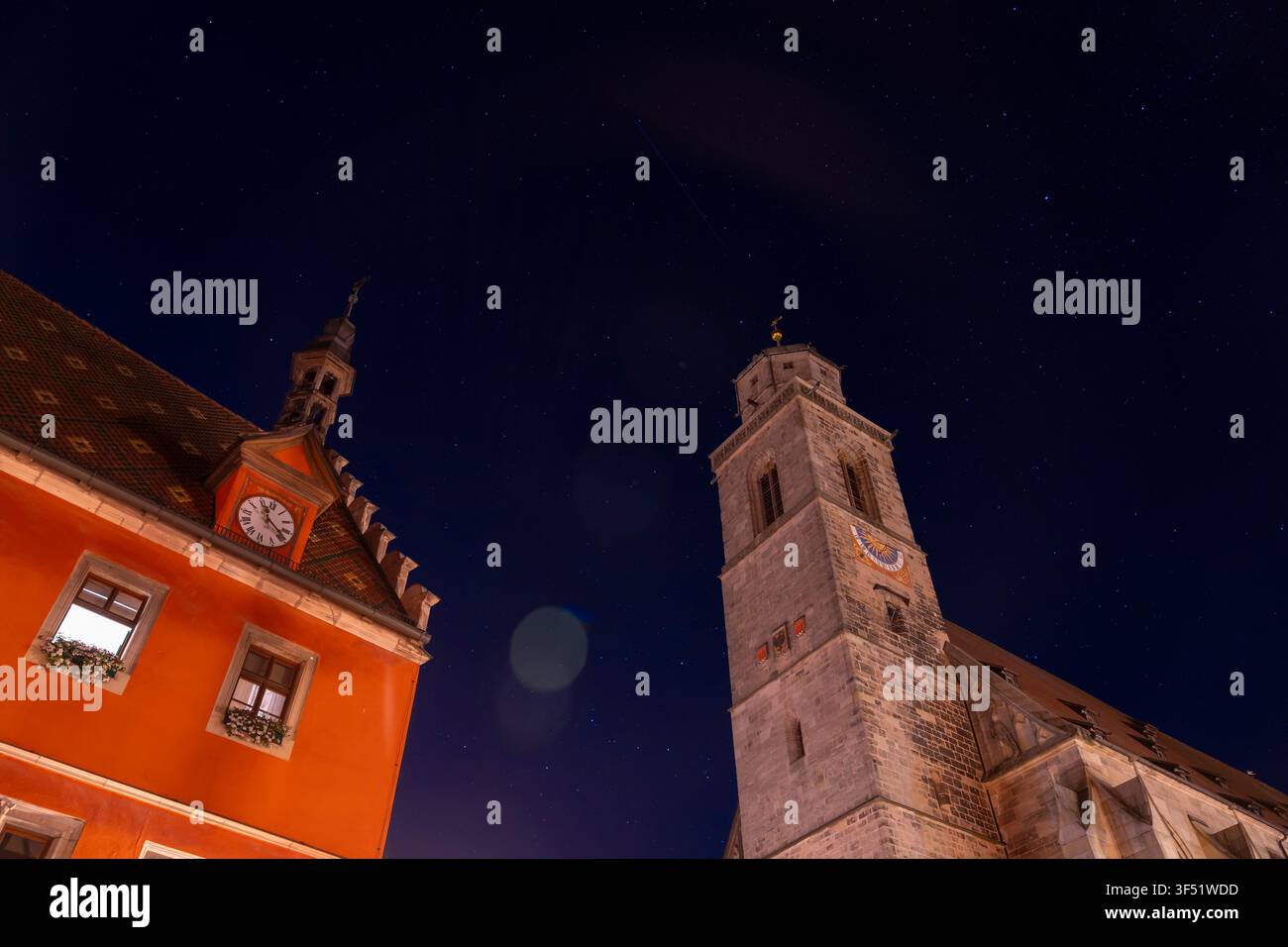 Una torre dell'orologio e un edificio arancione si stagliano contro un cielo notturno stellato. Foto Stock