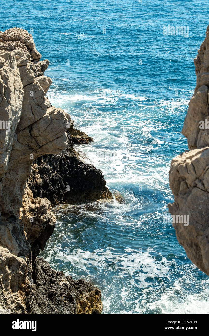 Schiuma di mare che turbina intorno alle aspre rocce costiere in Sicilia Foto Stock