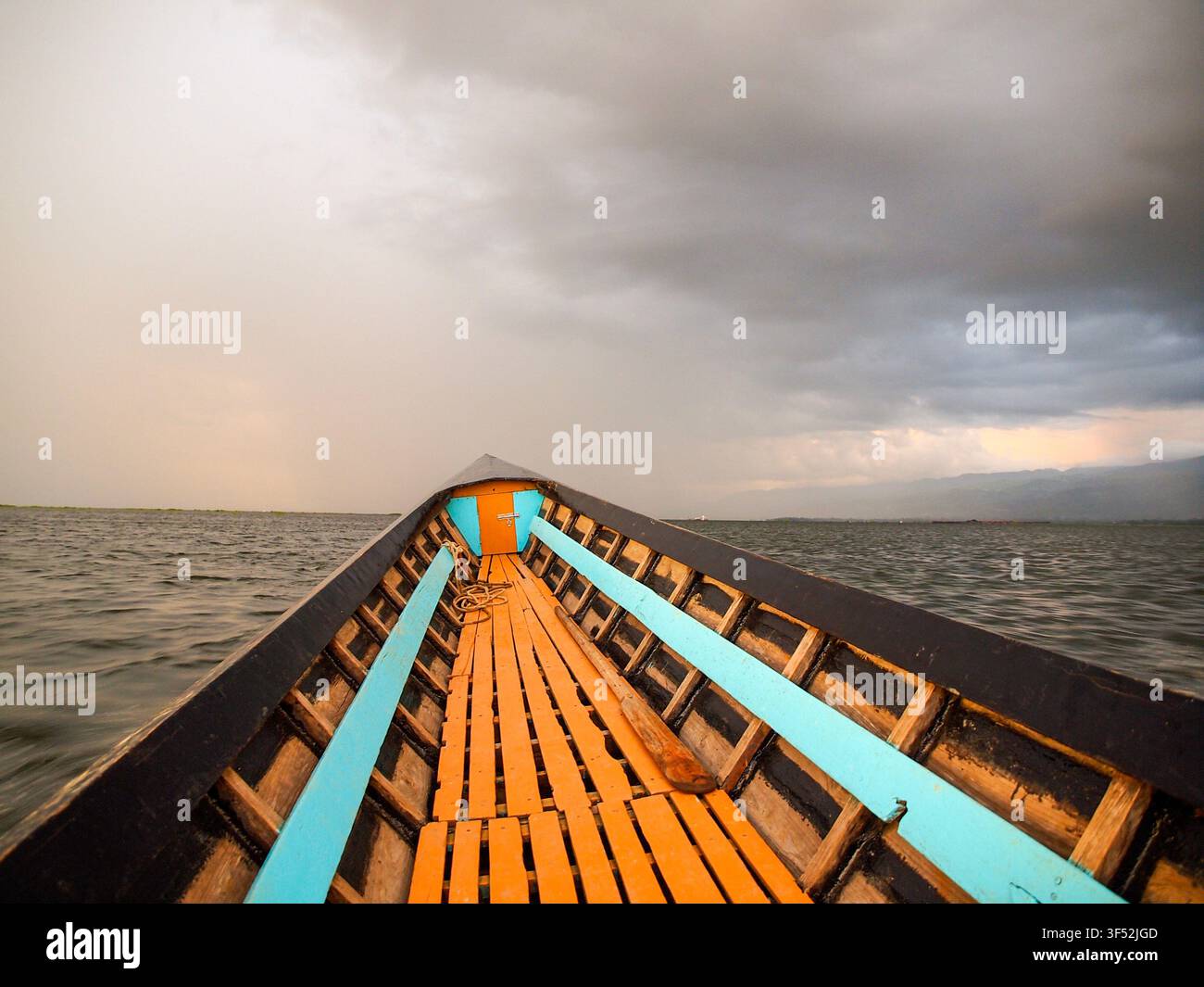 Prima di una barca sul lago Inle in Myanmar sotto un cielo nuvoloso e tempestoso al tramonto, scena di viaggio drammatica con luce atmosferica su acque calme e atmosfera di un villaggio galleggiante Foto Stock