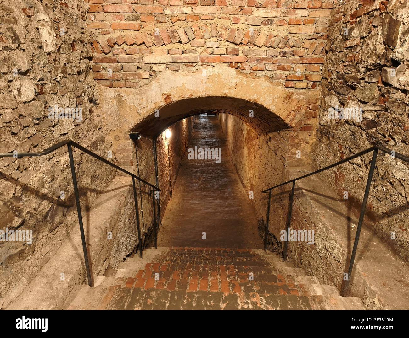 Antiche scale sotterranee in pietra e mattoni che conducono giù in un lungo e stretto passaggio tunnel di una fortezza medievale - Immagine stock catturata con smartphone
