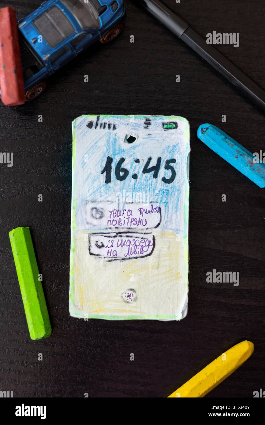 Smartphone di cartone fatto a mano creato da un bambino ucraino con notifica di allarme aereo. Concetto di infanzia durante la guerra, trauma psicologico e c Foto Stock