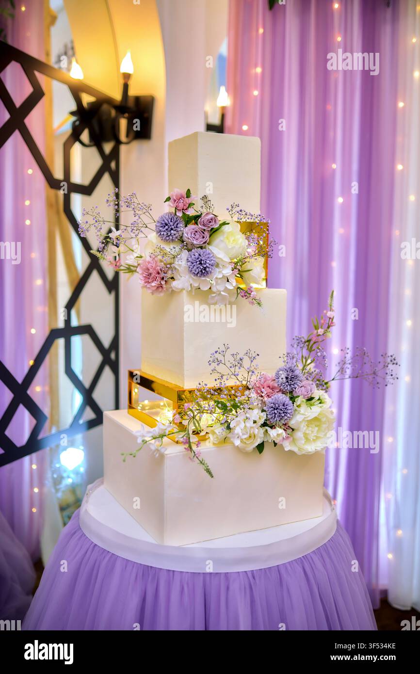Elegante torta nuziale bianca a tre piani con fiori freschi – Dessert per ricevimento di nozze di lusso Foto Stock