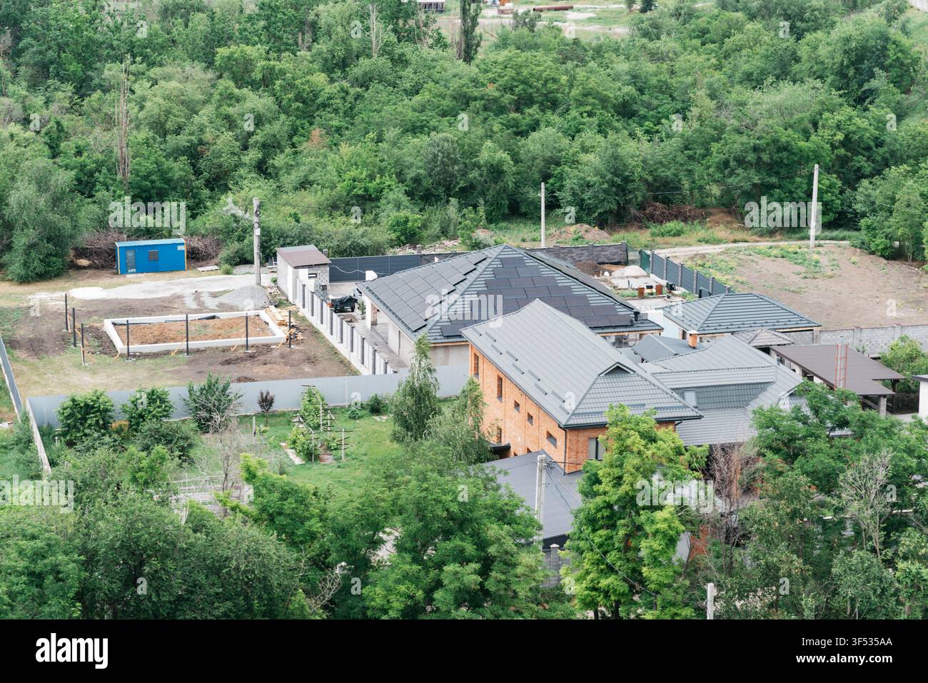 Vista elevata di case residenziali moderne con tetti grigi circondate da alberi verdi fitti e giardini in un quartiere suburbano tranquillo. Paesaggio estivo con case private, natura e ambiente di vita tranquillo. Foto Stock
