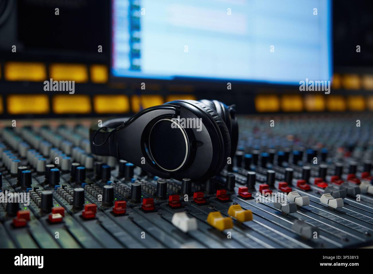 Cuffie appoggiate su una console di mixaggio sotto uno schermo morbido Foto Stock