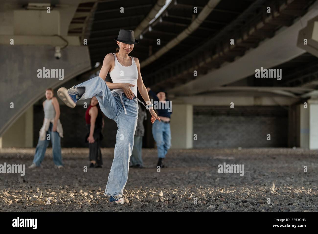 Donna con cappello fedora che balla per strada sotto un ponte Foto Stock
