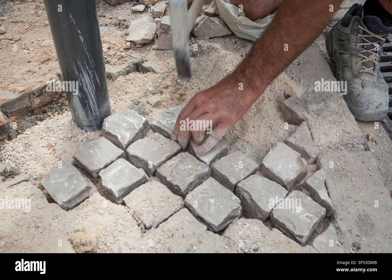 Muratore che ripara uno strato di pavimentazione portoghese Foto Stock