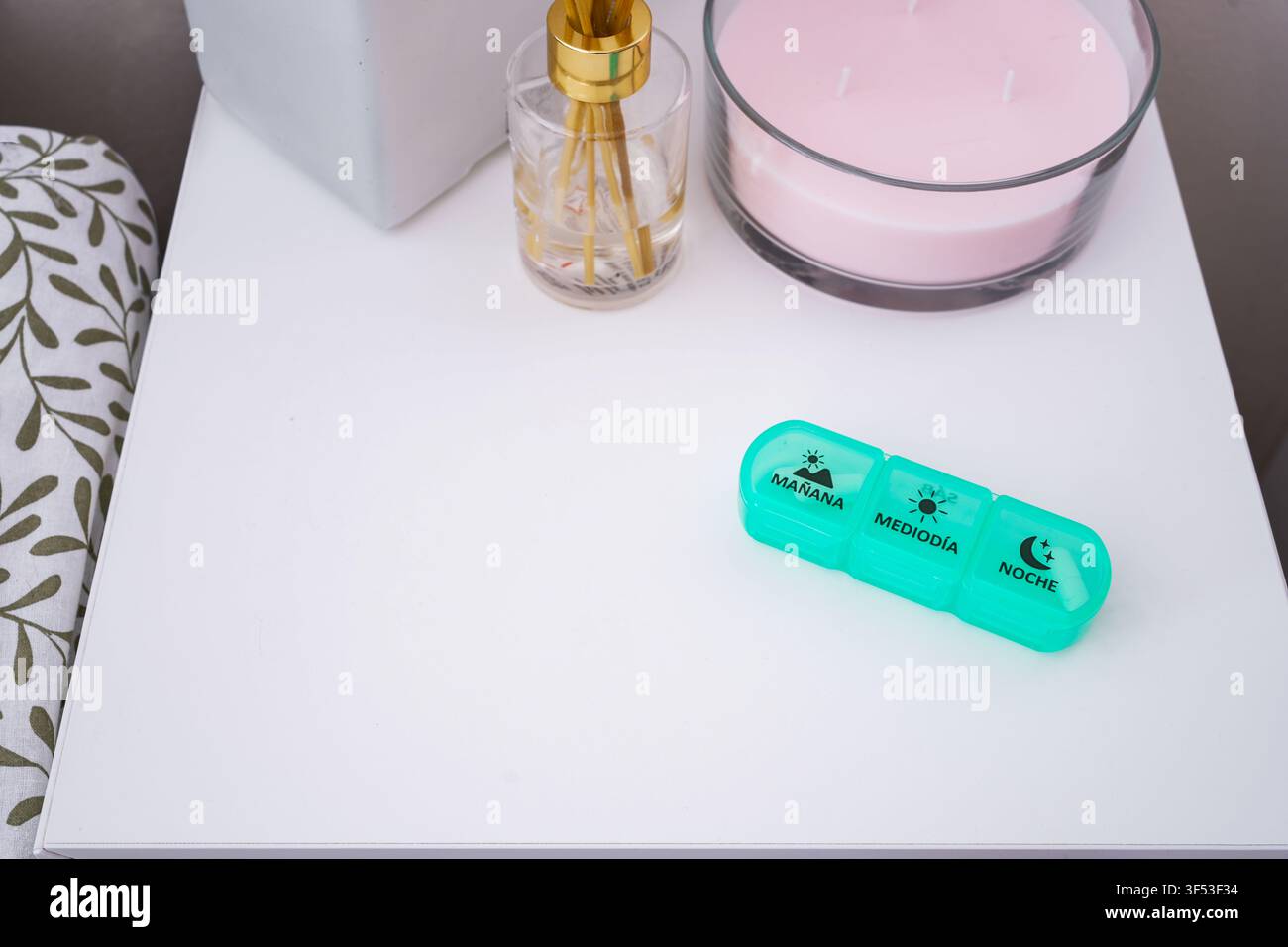 Un vivace organizzatore di pillole si trova su un comodino pulito accanto a una candela rosa calmante e a decorazioni eleganti, creando un'atmosfera calda perfetta per le routine notturne. Foto Stock