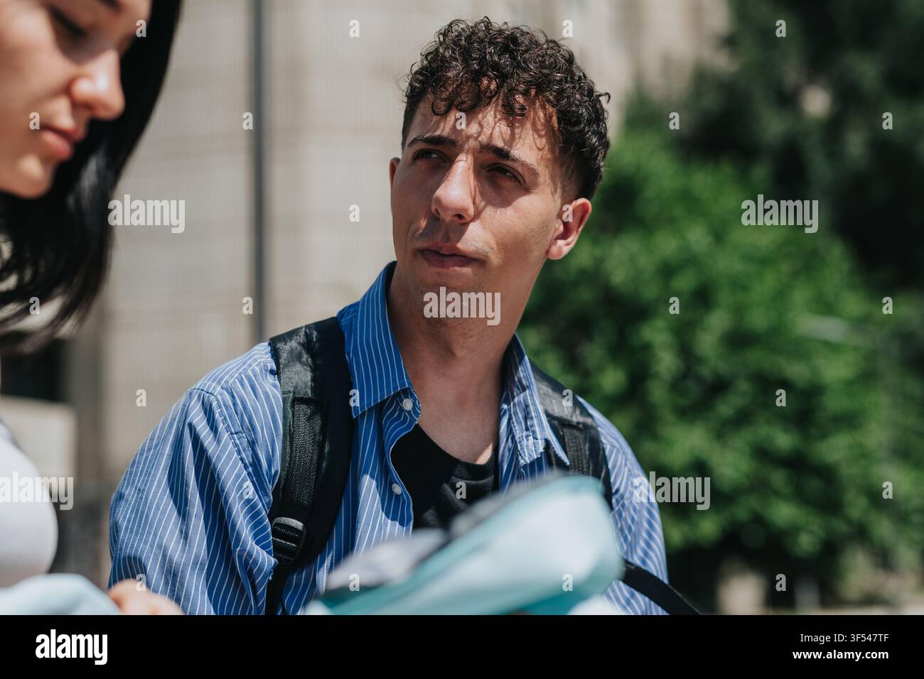 Studente maschio con zaino che studia all'aperto nel campus con un compagno di classe e materiale di studio Foto Stock