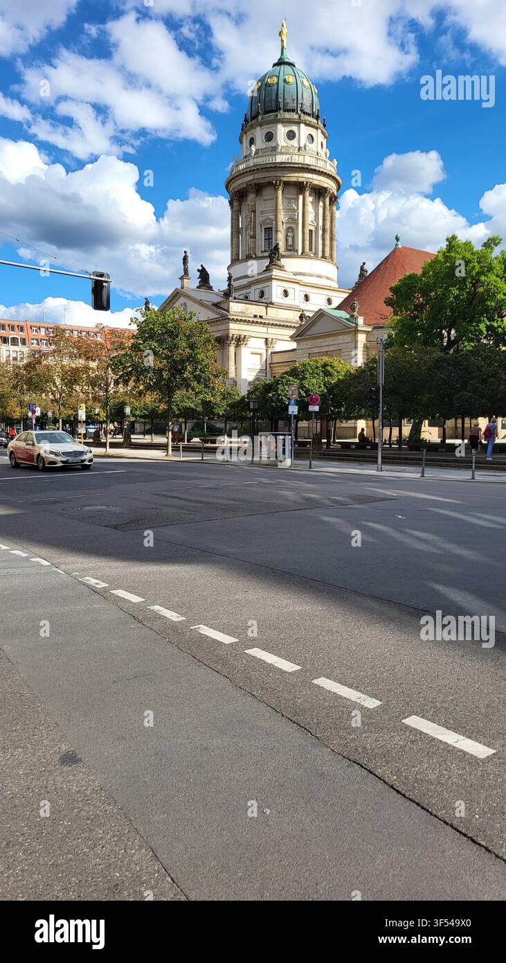 Duomo francese (cattedrale francese) visto attraverso una strada cittadina a Gendarmenmarkt a Berlino, Germania, sotto un cielo blu brillante con nuvole sparse. - Immagine stock catturata con smartphone