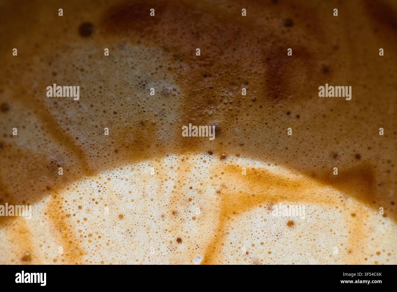 Vista macro di caffè appena preparato che mostra crema strutturata, minuscole bolle d'aria e motivi vorticosi di schiuma marrone sulla superficie di una bevanda calda Foto Stock