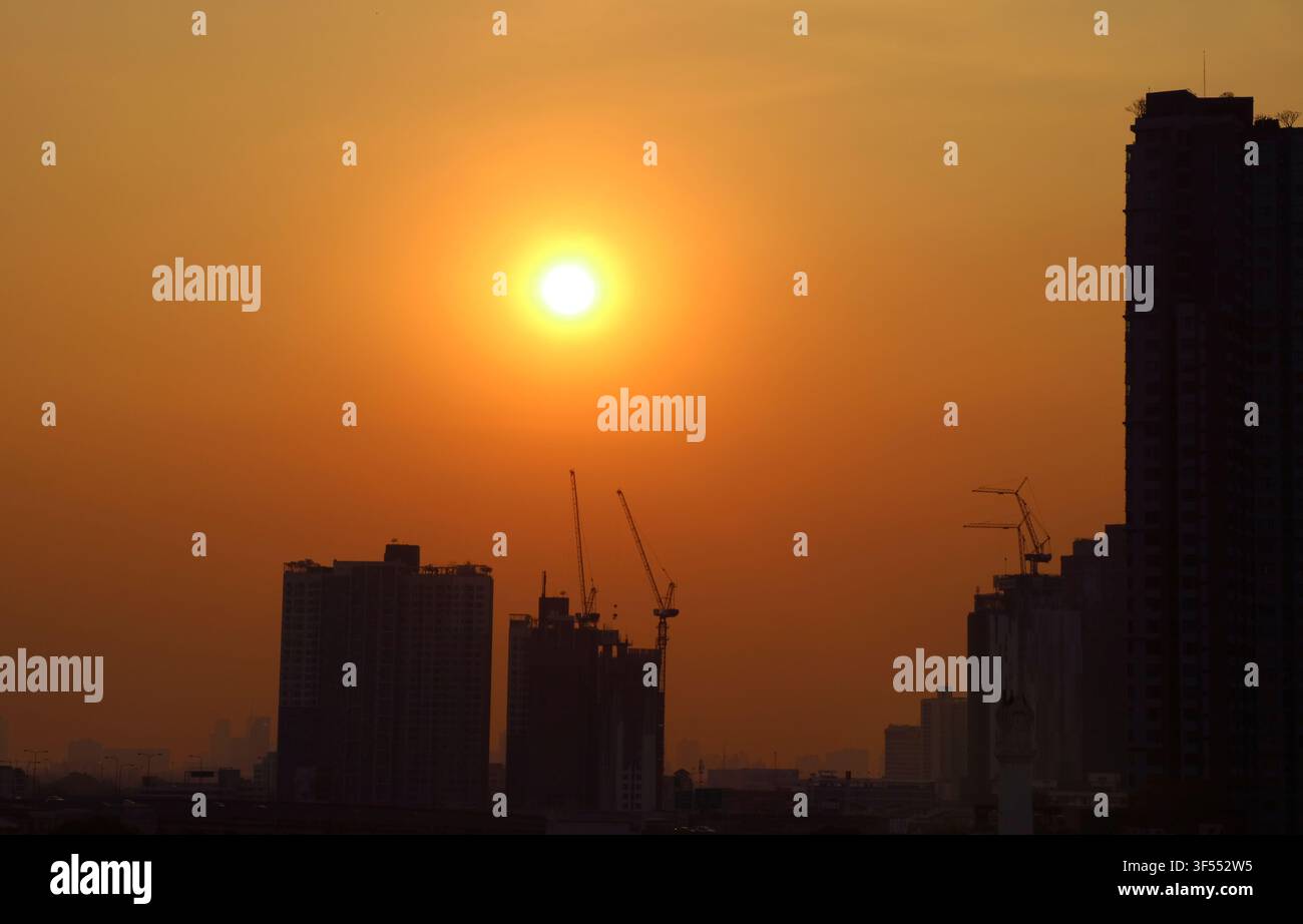 Sole luminoso che splende su un cielo arancione dorato sopra gruppi di grattacieli Foto Stock