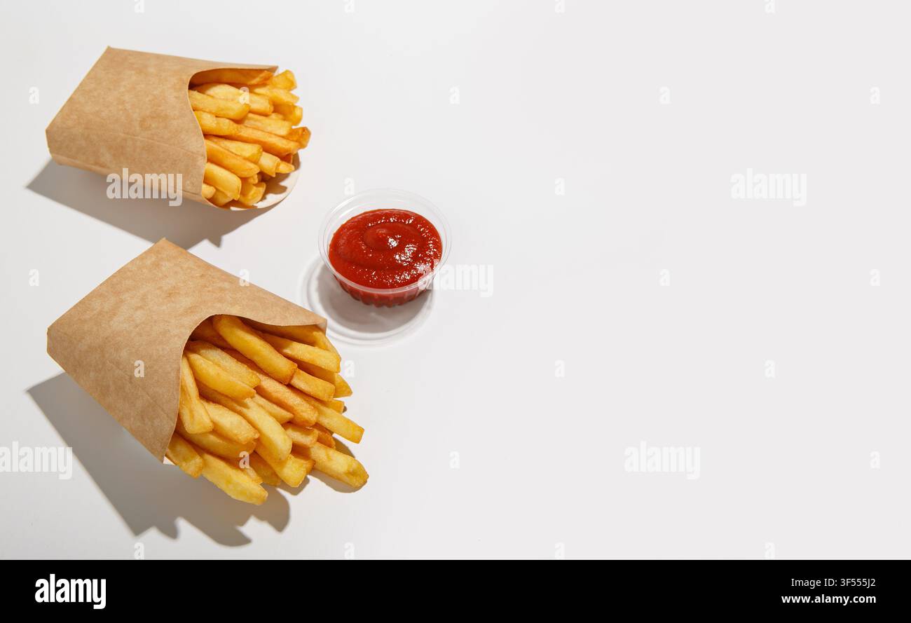 Ordine del cliente e consegna veloce di cibo a domicilio. Patatine fritte in confezione di cartone ecologico e ketchup al pomodoro in contenitore di plastica con ombra, isolato su bianco Foto Stock