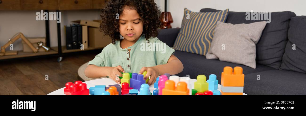 Un ragazzo afroamericano allegro gioca con blocchi da costruzione colorati nel suo appartamento accogliente, banner Foto Stock