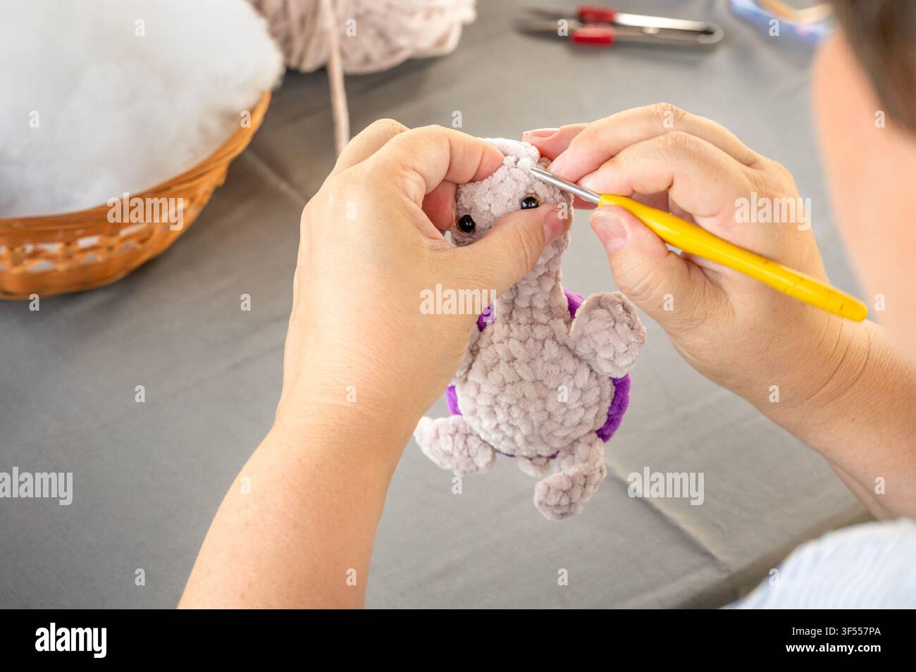 Mani di un'artigiana che cuce una testa di tartaruga di peluche morbida usando un uncinetto. Vista dettagliata della creazione di un giocattolo amigurumi fatto a mano durante un corso di maestro artigiano Foto Stock