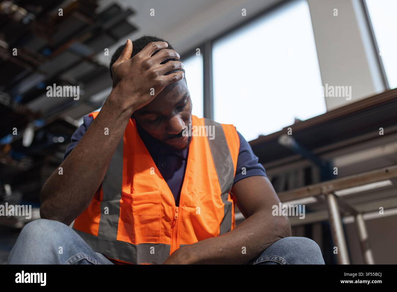 Lavoratore di fabbrica in burnout con la testa tra le mani dopo un lungo turno. Sperimenta stress e affaticamento a causa del suo lavoro. Foto Stock