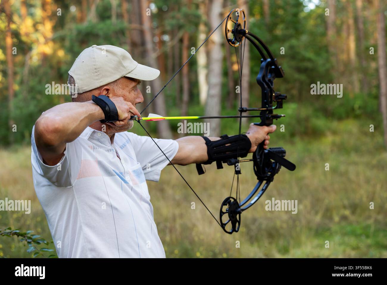 Uomo anziano che pratica il tiro con l'arco con arco composto nella foresta Foto Stock