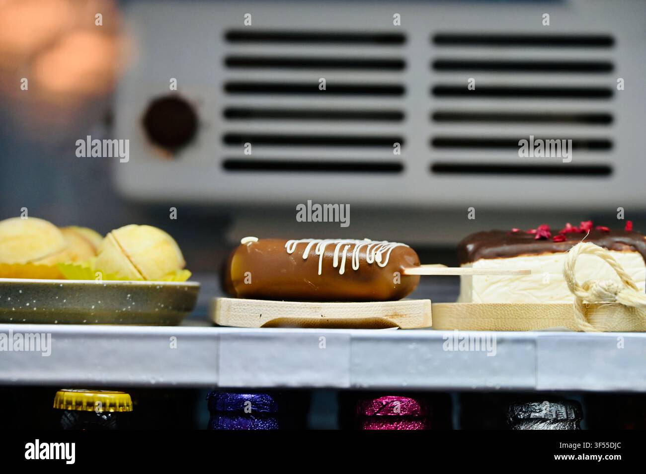 Vista interna di un frigorifero commerciale moderno o di una vetrina rifornita di deliziosi dessert, prodotti da forno, rotoli di waffle e bottiglie sugli scaffali sotto una luce LED brillante. Foto Stock