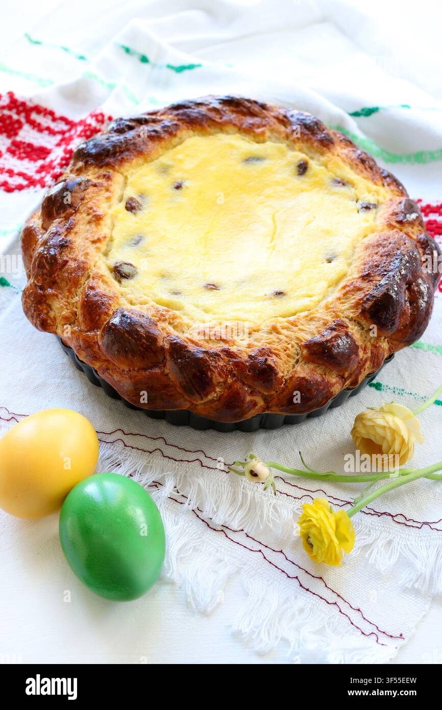 Tradizionale torta pasquale rumena Pasca con formaggio dolce e uvetta, decorata con uova colorate e fiori primaverili. Tradizione pasquale dell'Europa dell'Est Foto Stock