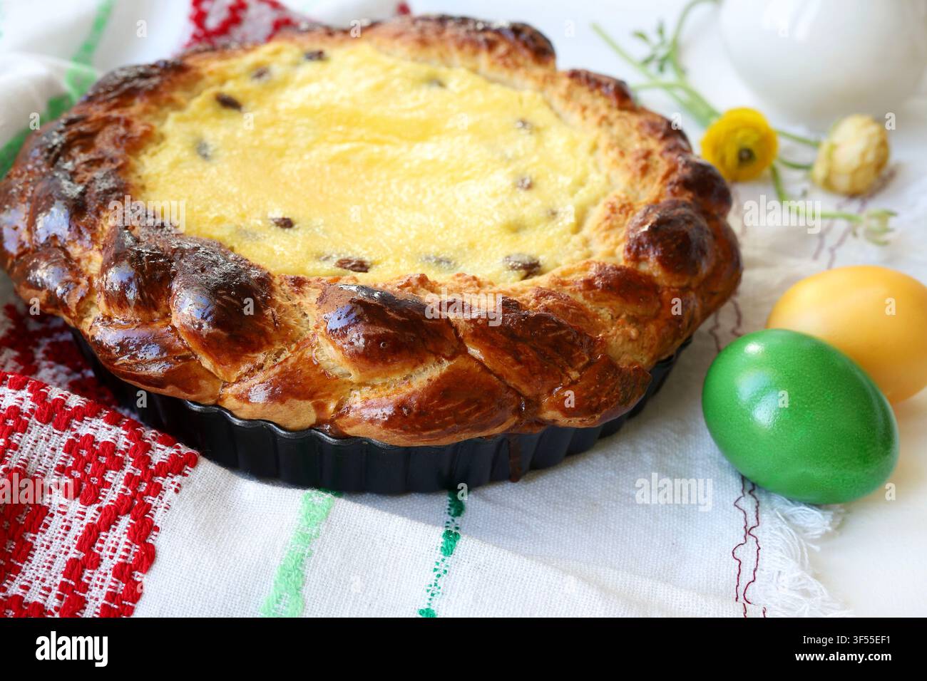 Tradizionale torta pasquale rumena Pasca con formaggio dolce e uvetta, decorata con uova colorate e fiori primaverili. Tradizione pasquale dell'Europa dell'Est Foto Stock