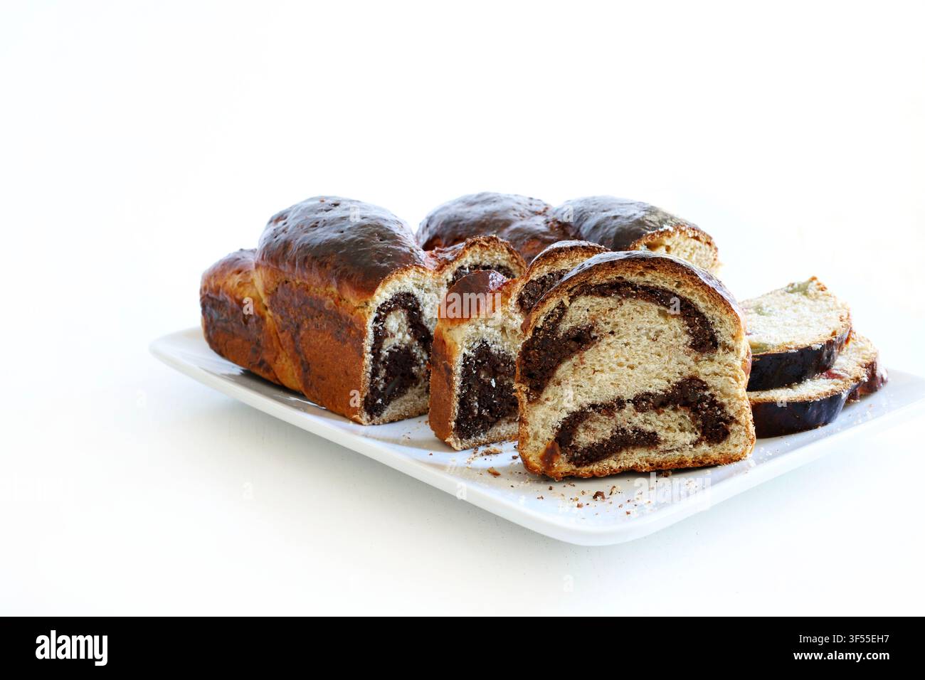 Cozonac rumeno tradizionale per le festività con vortice di noci e cacao su un piatto bianco, isolato su tavolo bianco. Concetto di stagione festiva. Foto Stock