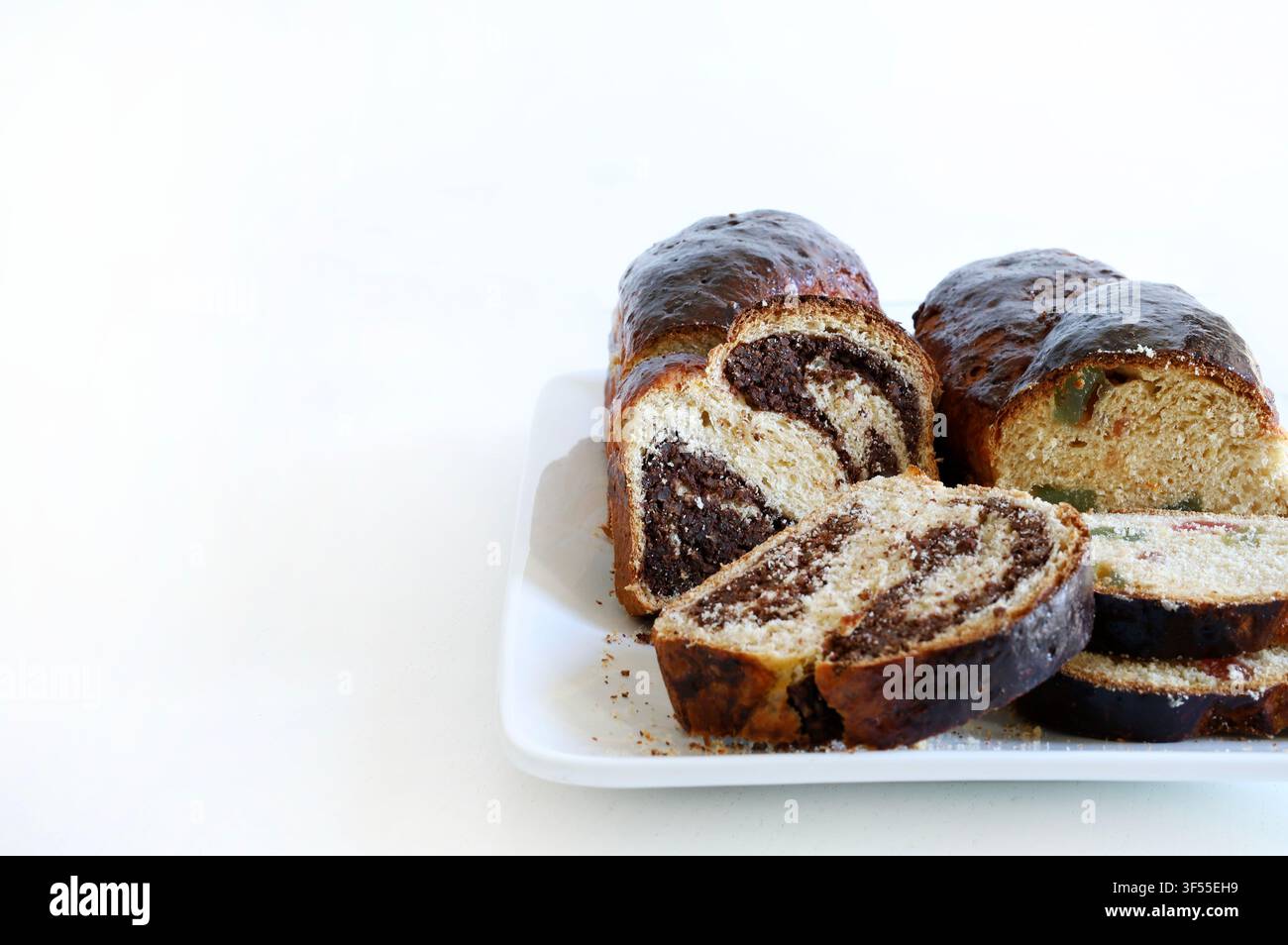 Cozonac rumeno tradizionale per le festività con vortice di noci e cacao su un piatto bianco, isolato su tavolo bianco. Concetto di stagione festiva. Foto Stock