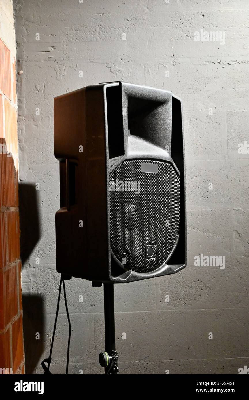 Prima piano di un altoparlante audio da palco professionale nero montato su un supporto metallico davanti a un muro di cemento ruvido in un luogo o in uno studio. Foto Stock