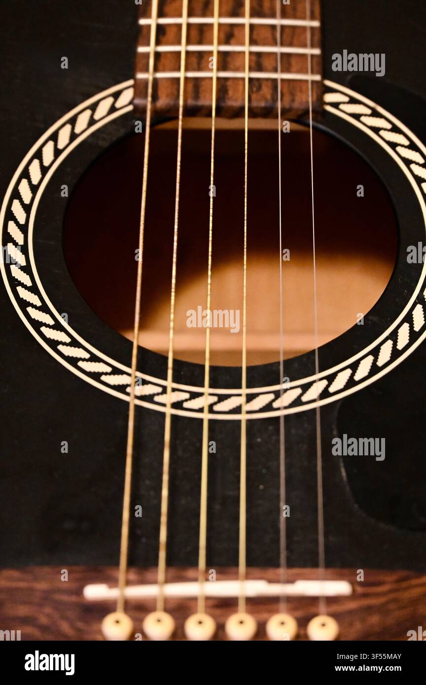Vista ravvicinata della rosetta con motivo a corda decorativa nell'apertura acustica di una chitarra, con corde metalliche, tastiera e ponte su un corpo scuro. Foto Stock