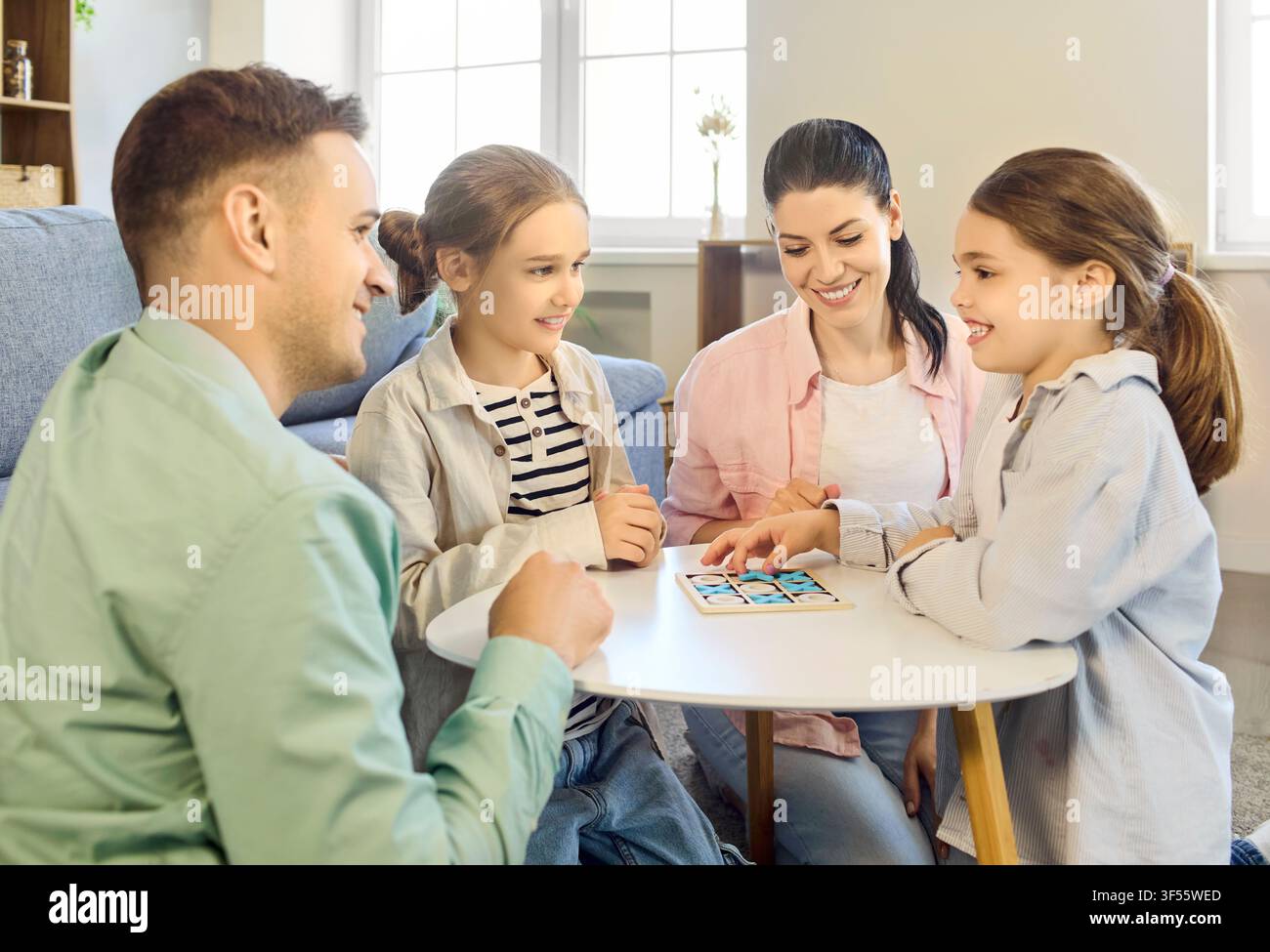 Famiglia sorridente che gioca a un gioco da tavolo a casa, genitori e bambini che si godono del tempo di qualità Foto Stock