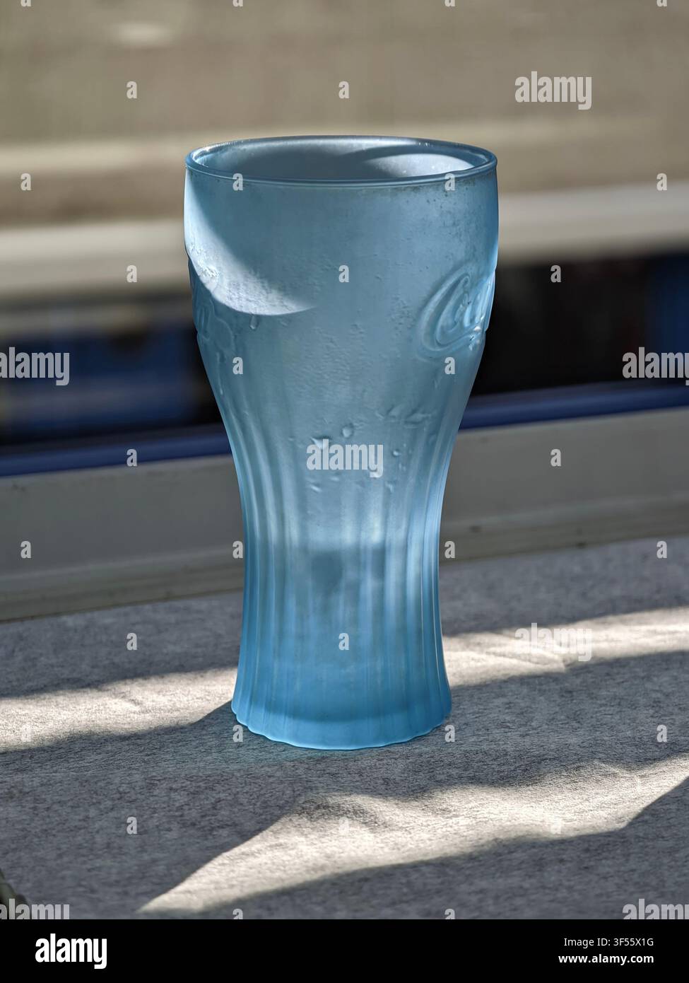 Pforzheim, Germania, 30 luglio 2026 Primo piano di un bicchiere di vetro blu coperto da gocce di condensa, posizionato su un patio esterno in cemento in una luminosa estate Foto Stock