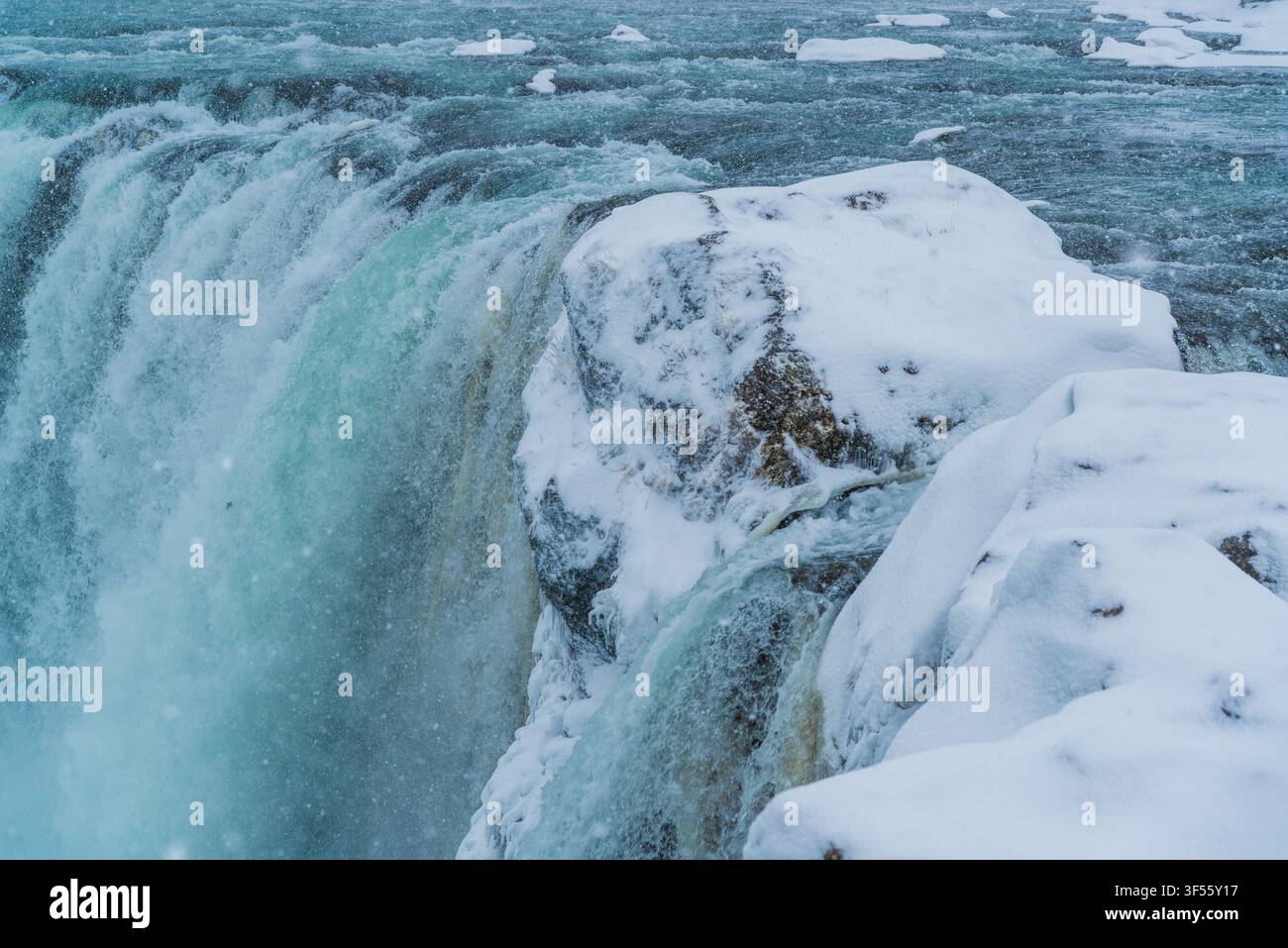 Prima piano di una cascata invernale gelata con acqua che scorre a tutta velocità su formazioni rocciose coperte di neve in condizioni meteorologiche fredde Foto Stock