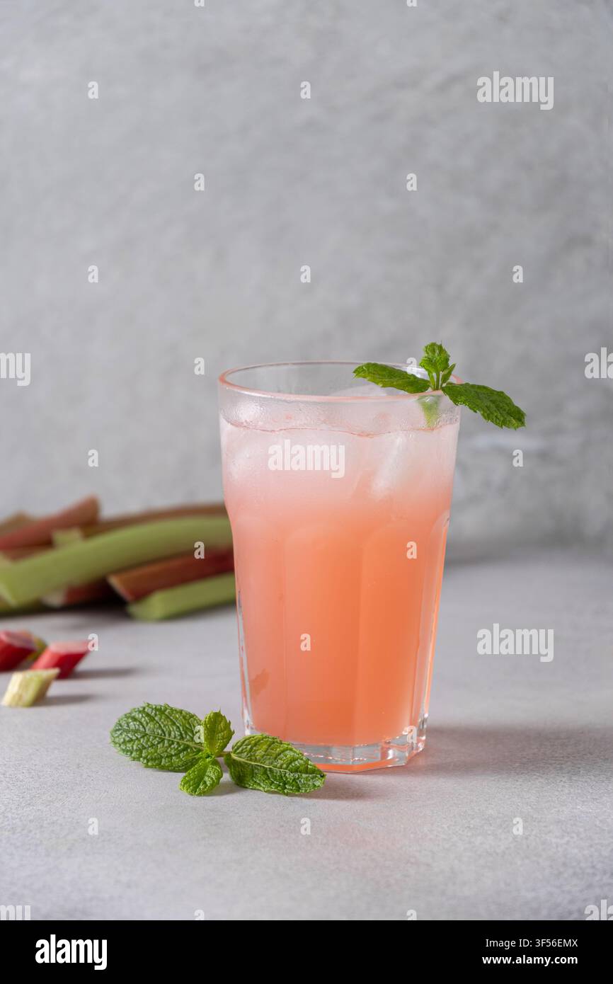 Limonata rinfrescante fatta in casa con rabarbaro, cubetti di ghiaccio e menta fresca servita in un bicchiere alto su sfondo di pietra chiara, bevanda estiva sana e stagionale. Ve Foto Stock